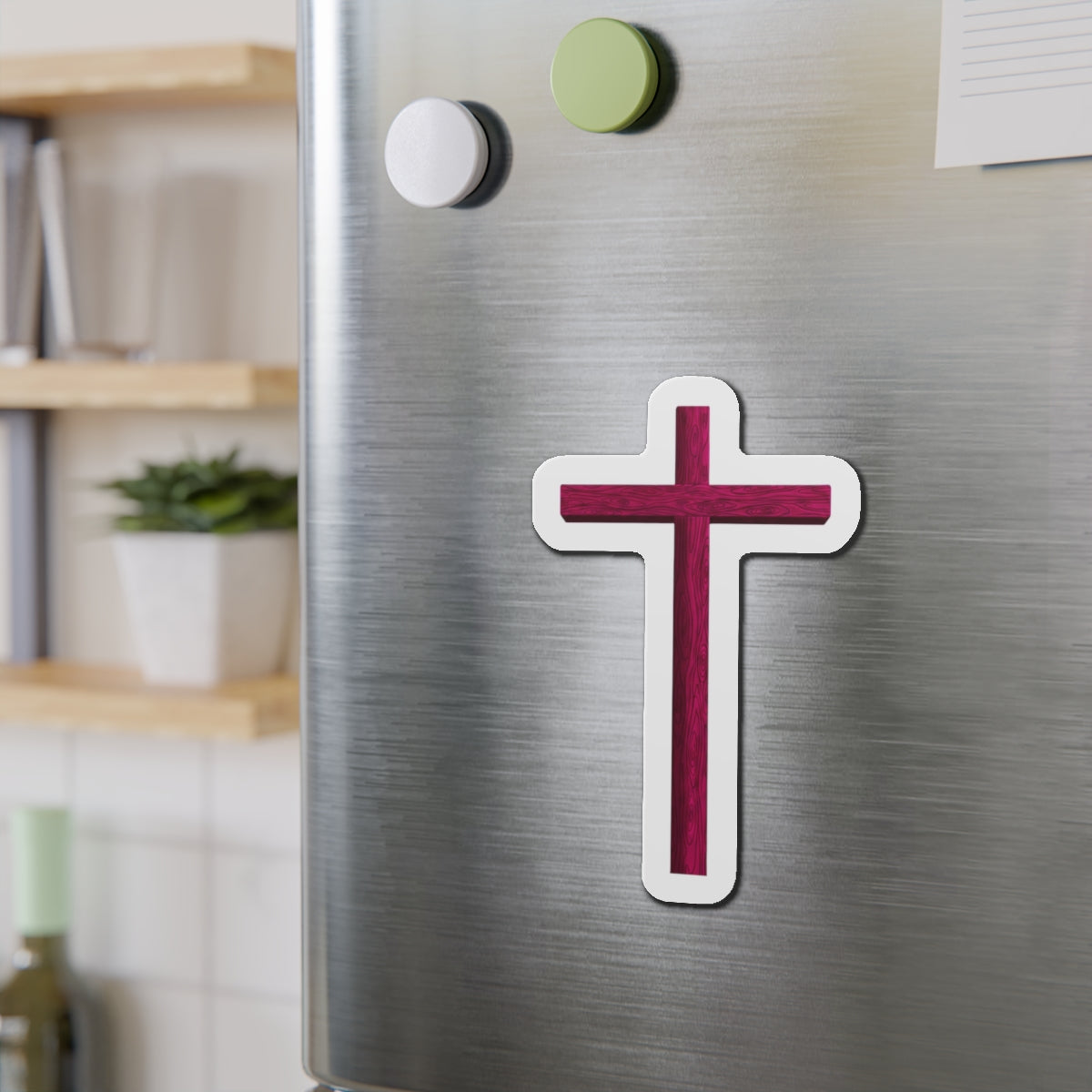 Cross-shaped magnet on a metallic surface with a blurred indoor background