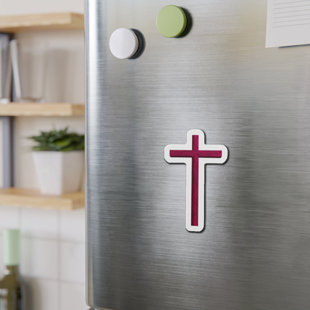 Cross-shaped magnet on a metallic surface with a blurred indoor background
